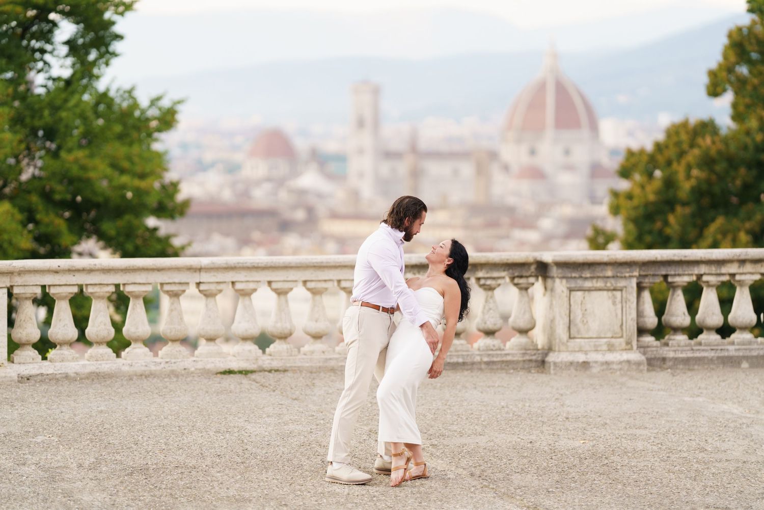 Romantic couple walking on a scenic overlook in Florence, Italy with the Duomo cathedral dome visible in background.