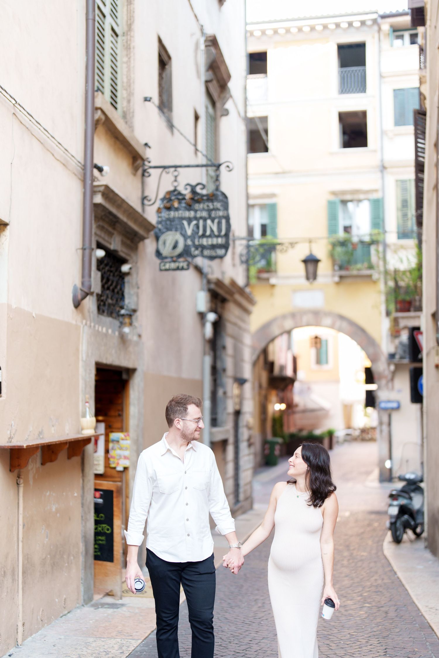 A couple walks hand in hand through a charming European cobblestone street lined with historic buildings.