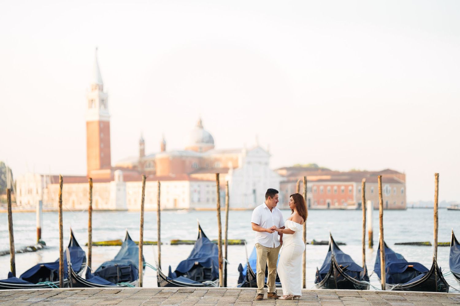 A panoramic view of gondolas moored along the Venice waterfront with San Giorgio Maggiore church in the background.