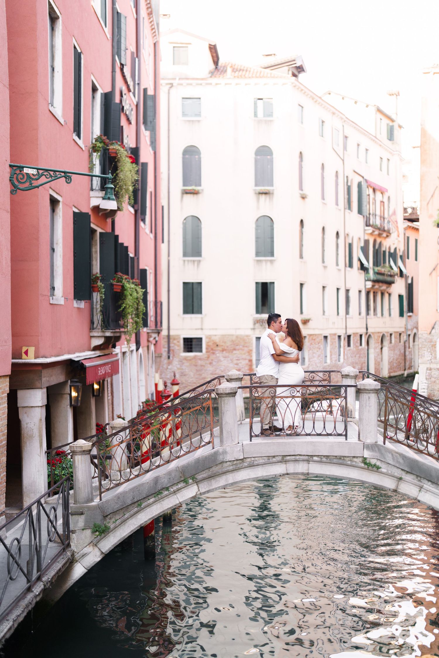 Scenic view of a narrow Venice canal with pink buildings and small bridges crossing over the waterway.