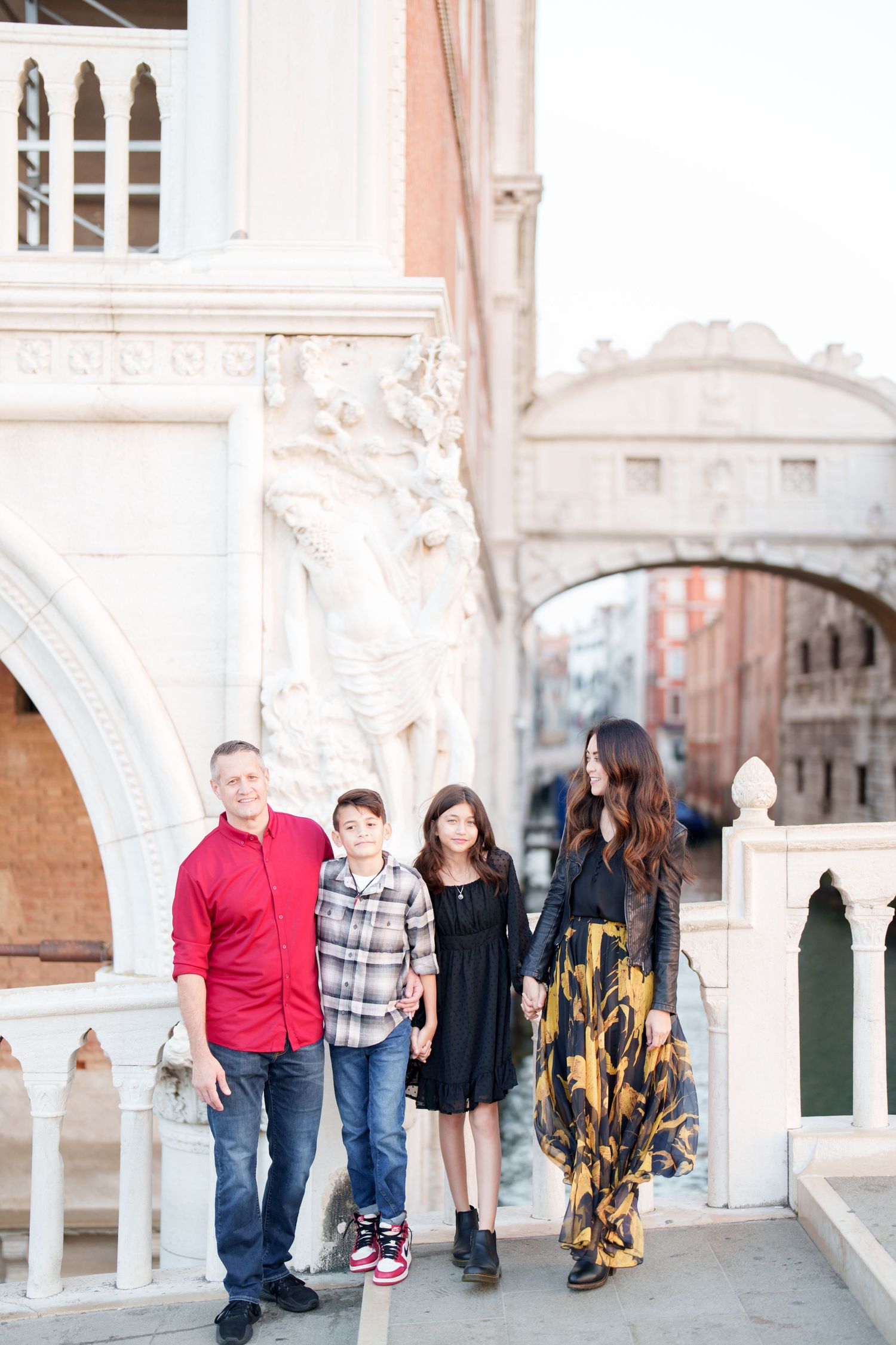 A group stands together on a bridge in Venice with ornate architecture and the Bridge of Sighs visible in the background.