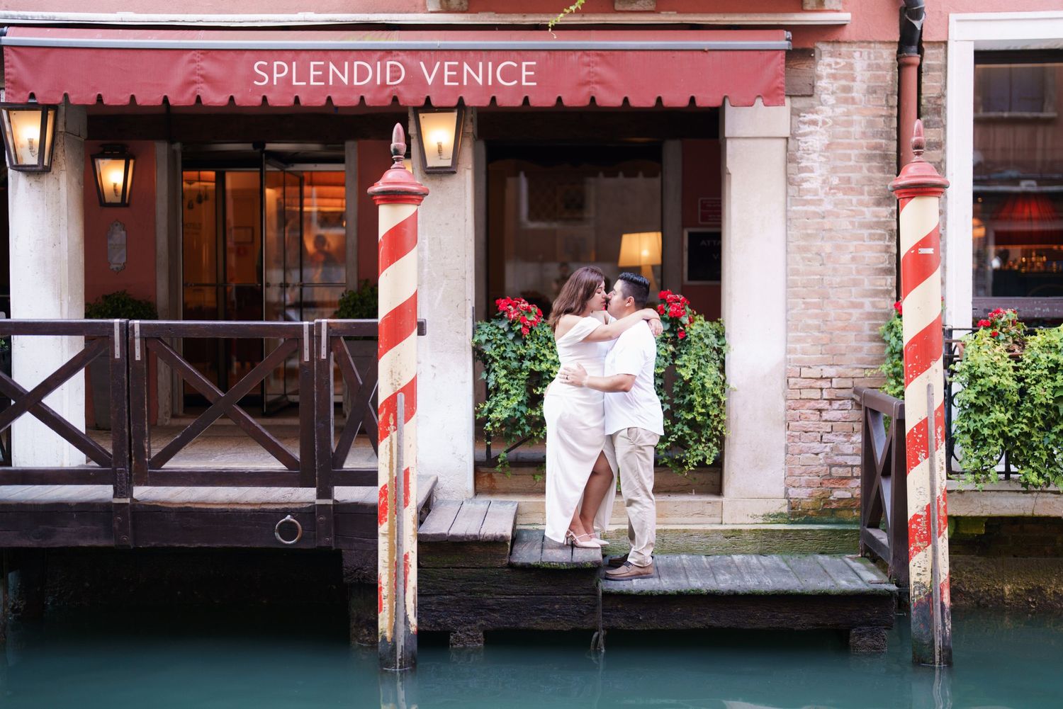 Red and white striped poles line the waterfront of a historic Venice canal with brick buildings and wooden docks.