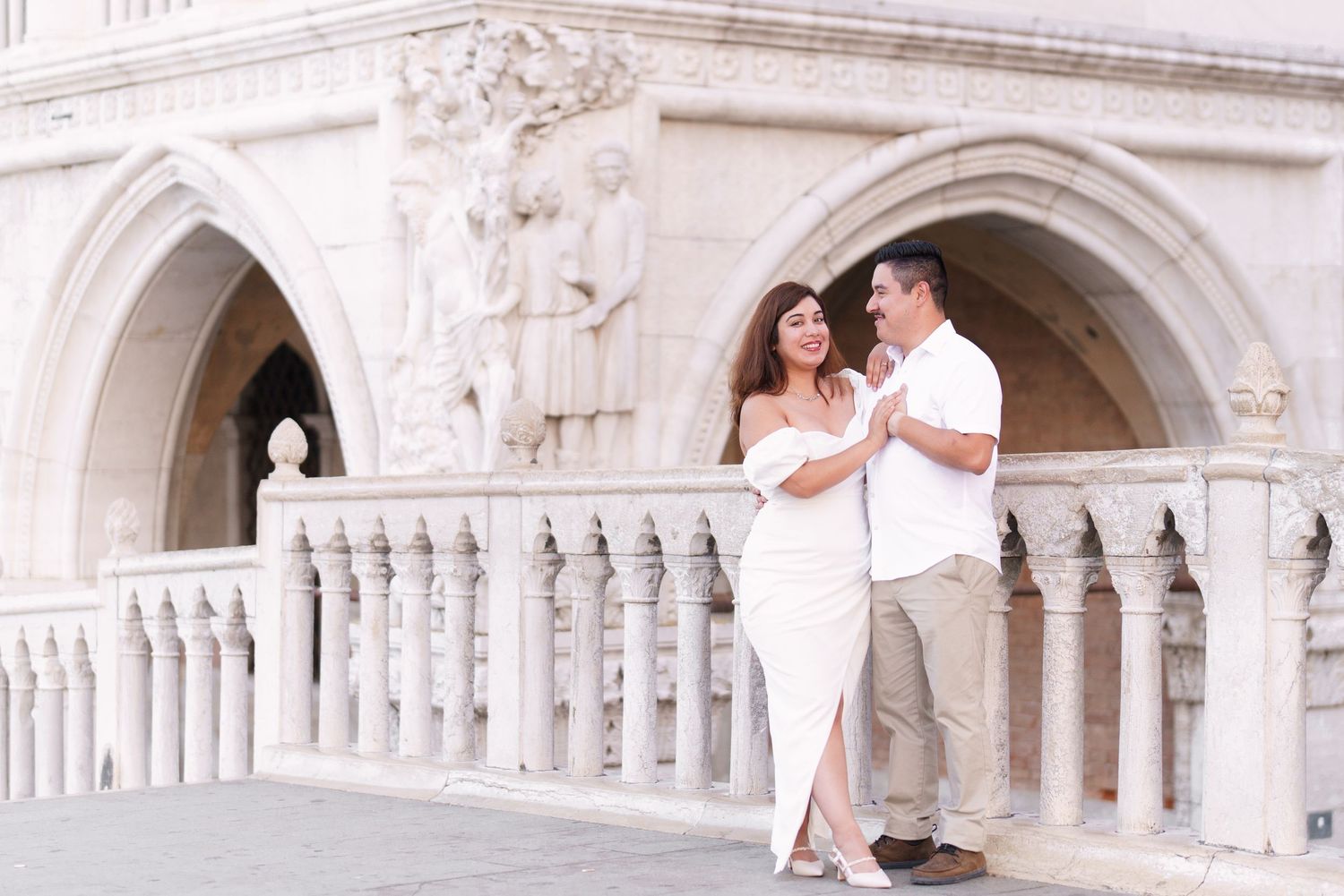 A couple shares a romantic moment under a white stone archway in Venice, Italy.