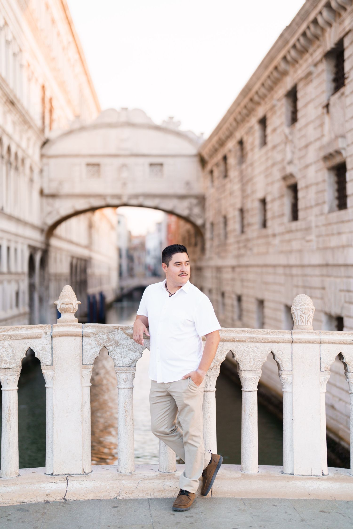 Child in light-colored clothing sits on white stone railing in historic European architecture setting at sunset.