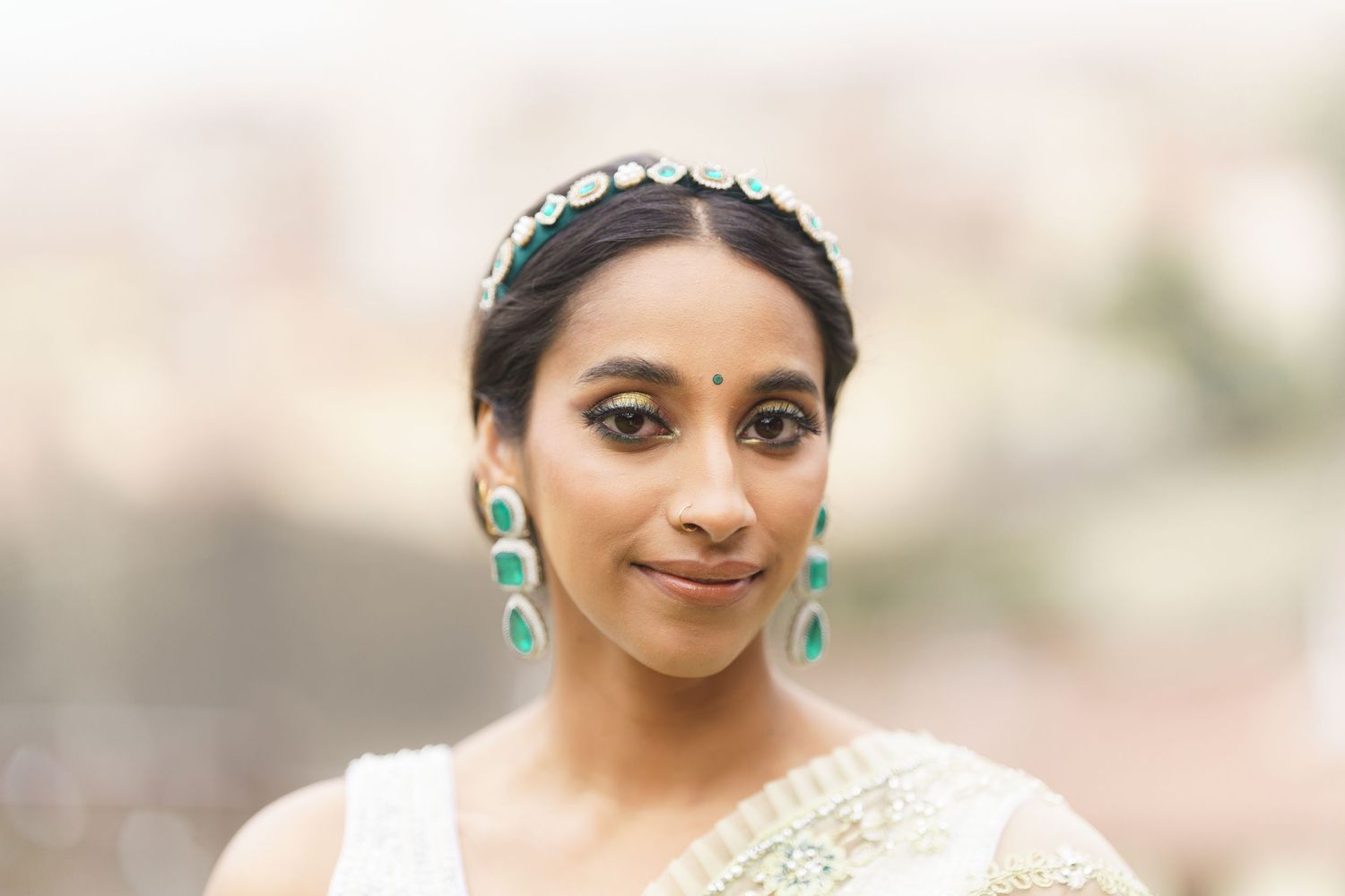 A person in traditional South Asian bridal attire with gold jewelry and a detailed embroidered outfit poses elegantly.
