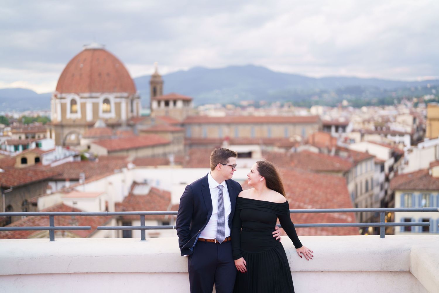 A couple shares a romantic moment on a rooftop terrace overlooking Florence's historic skyline and Duomo cathedral.