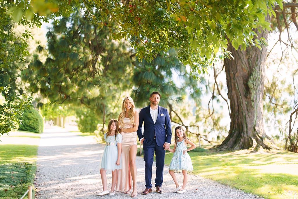 A family walks together down a tree-lined path on a sunny day in formal attire.