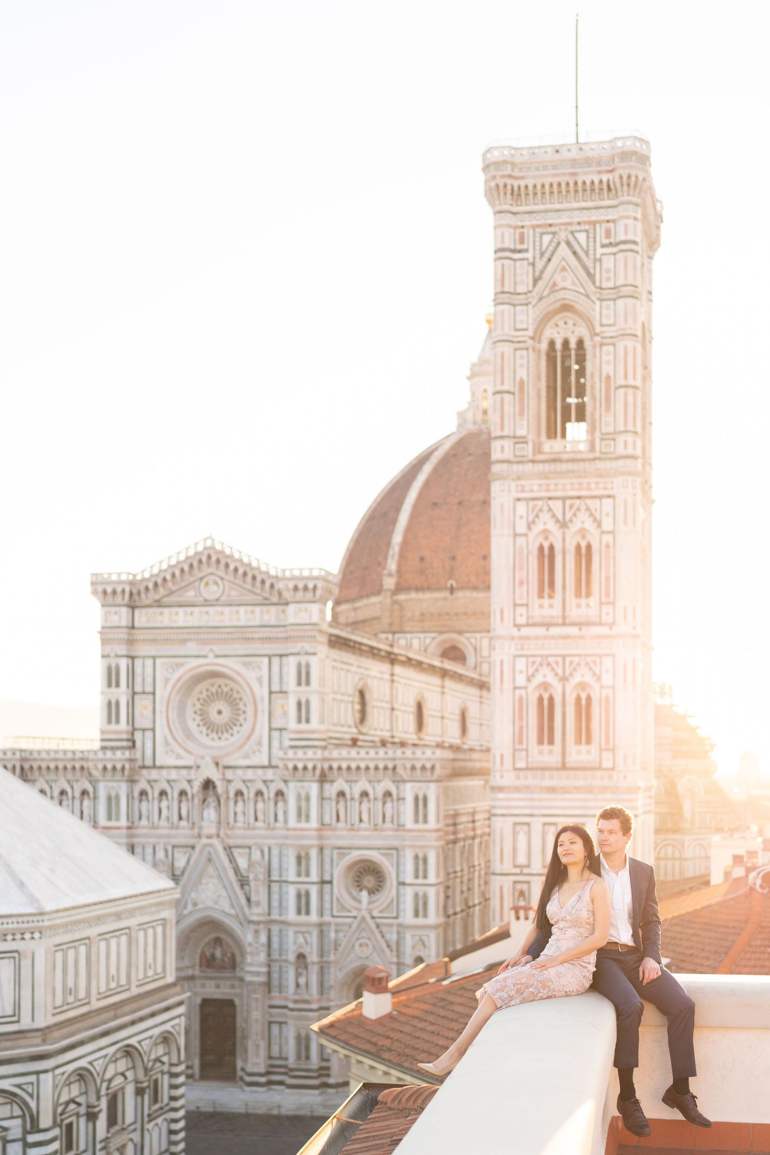 A couple sits on a rooftop overlooking the historic Florence Cathedral and Giotto's Bell Tower during golden hour.