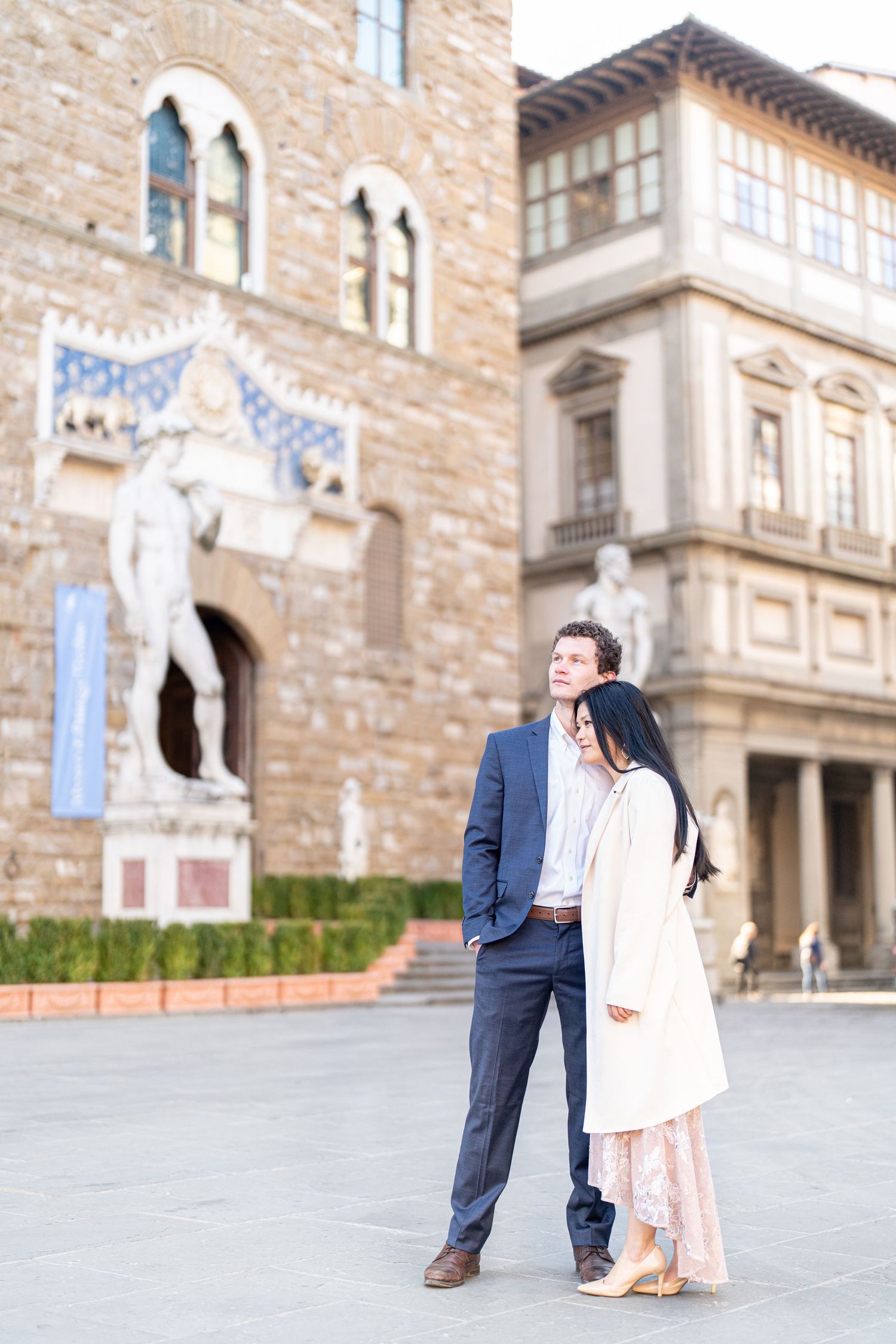 A couple stands together in front of a historic Italian building with stone walls and arched windows in Florence.