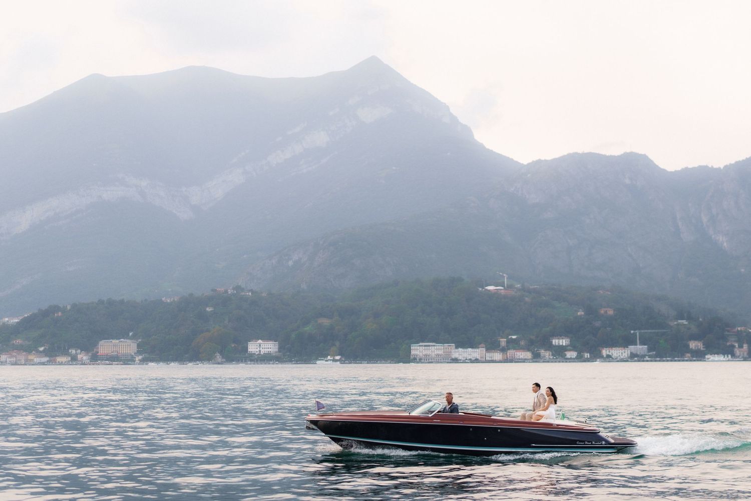 Panoramic view of a scenic mountain lake with boats and distant peaks under cloudy skies.