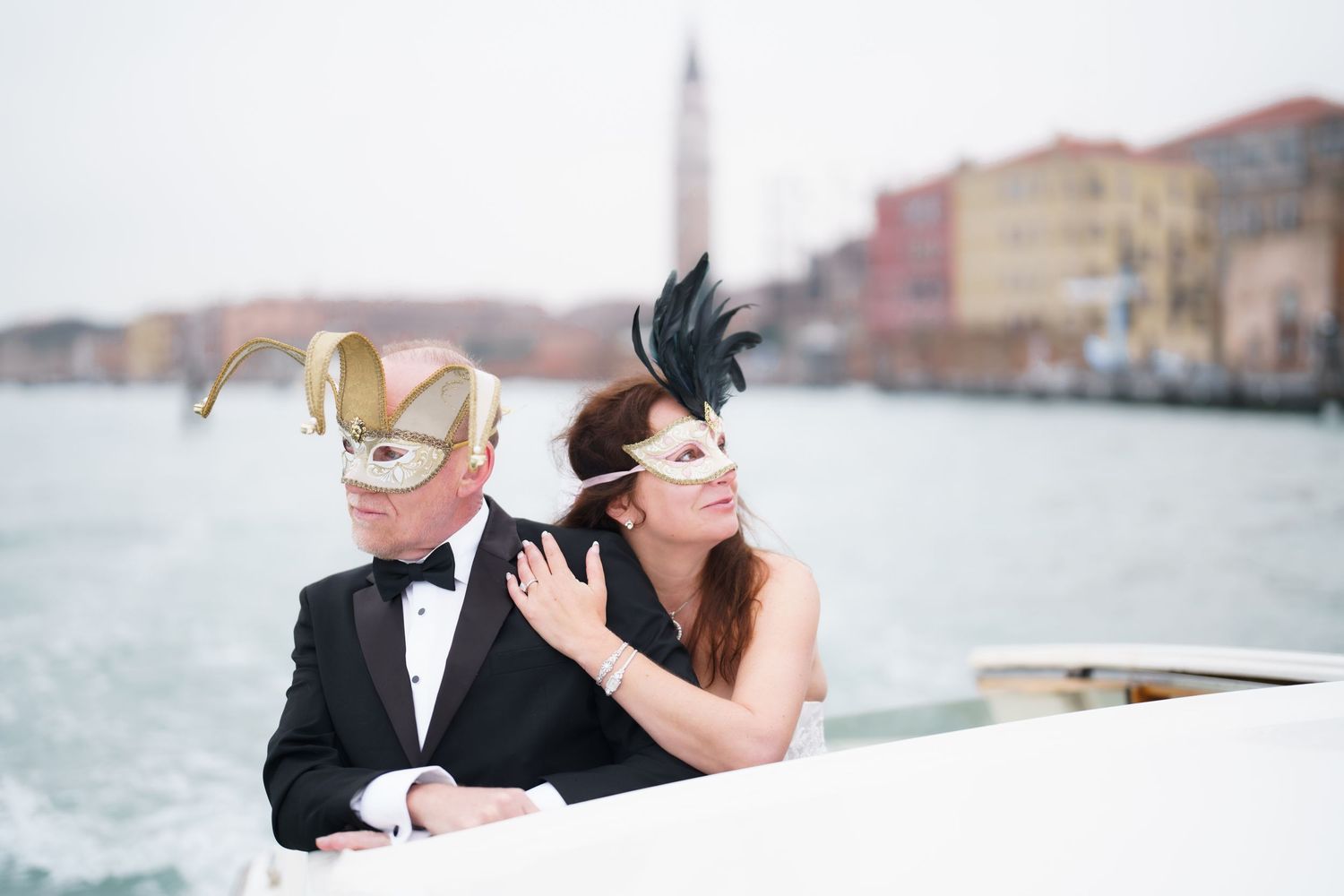 A romantic couple in formal attire embraces while kissing on a boat dock near the water at sunset.