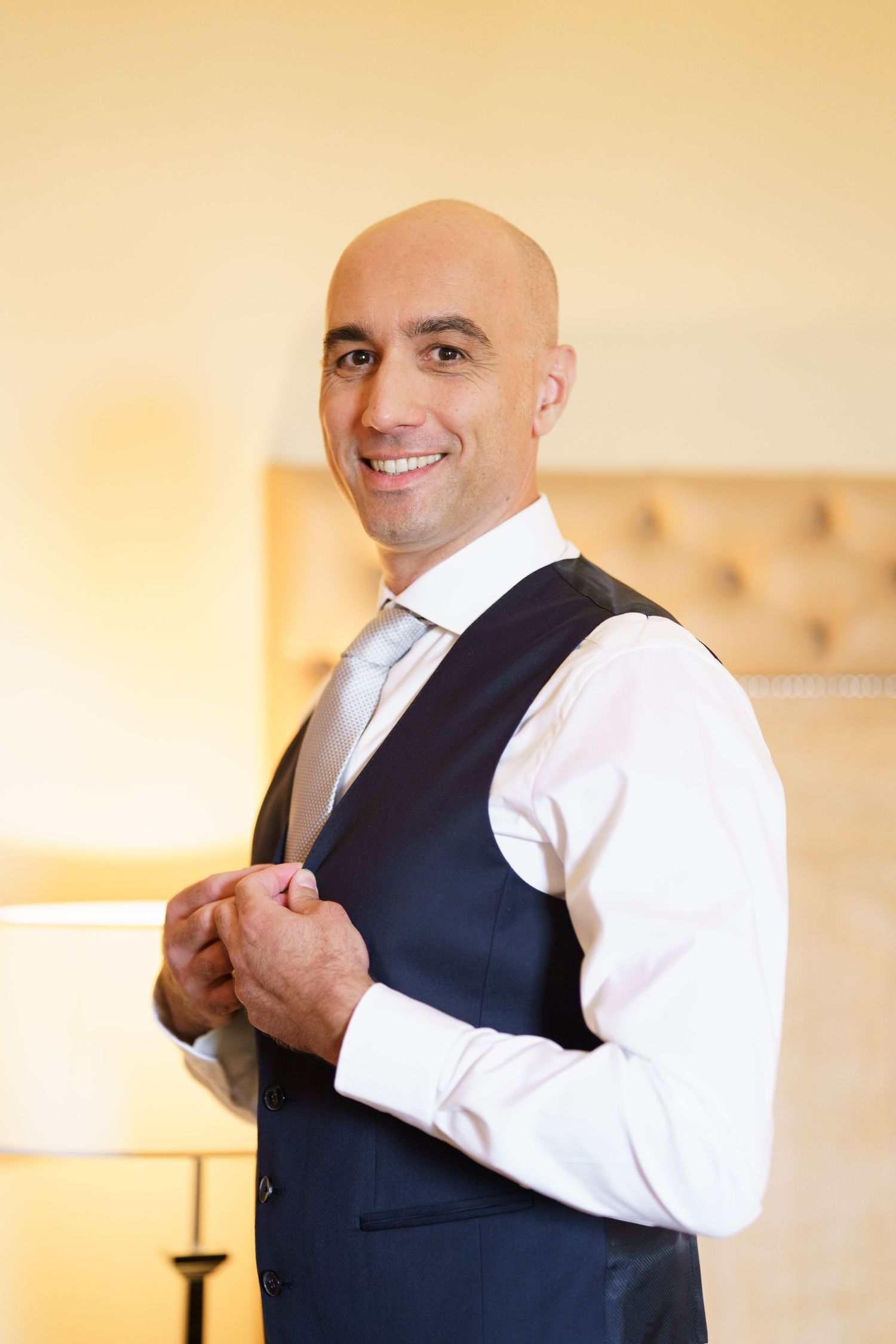 Man in vest and white shirt smiling while adjusting formal wear.