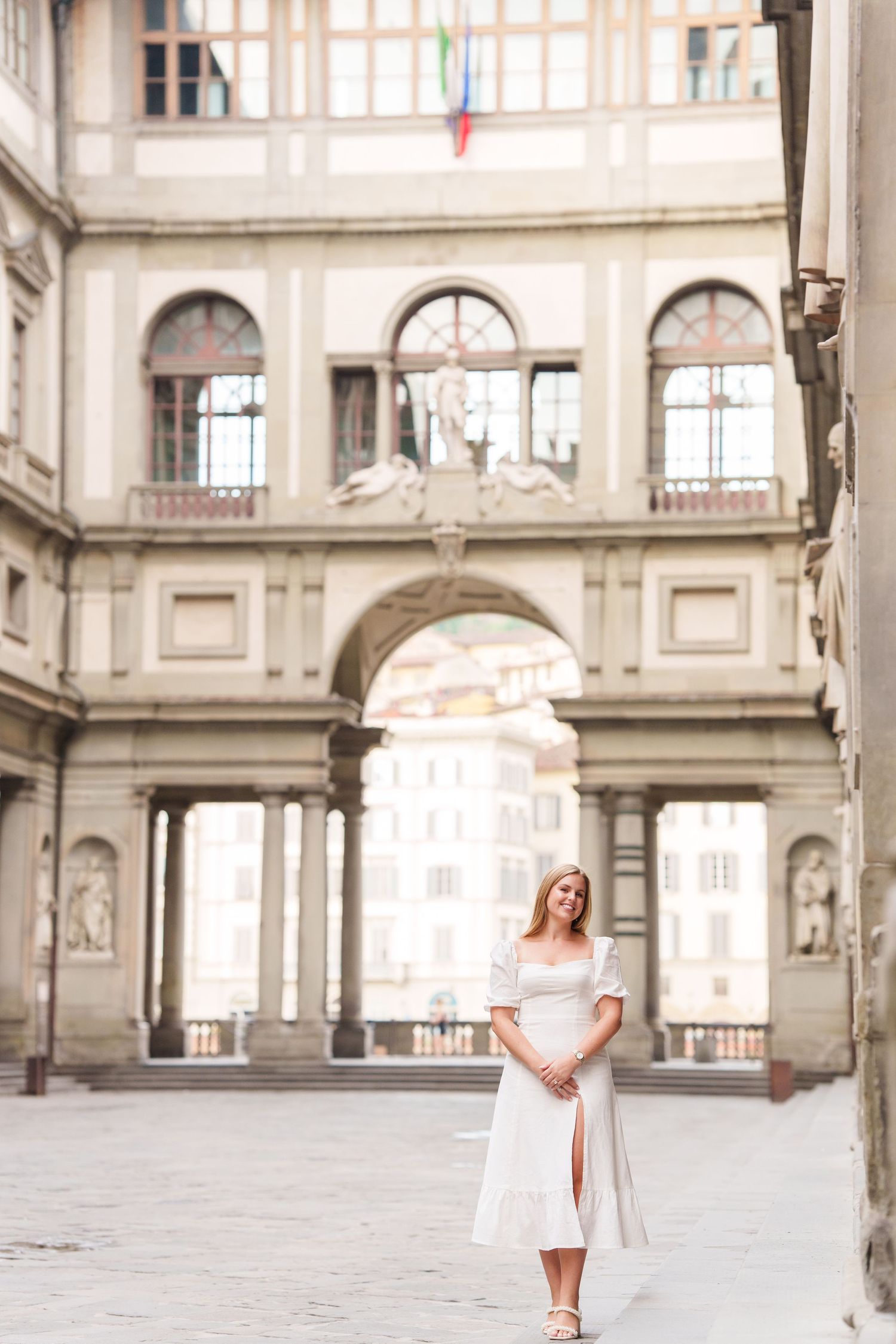 Woman in white dress poses gracefully in three different positions under historic stone archways of Uffizi Gallery in Florence.