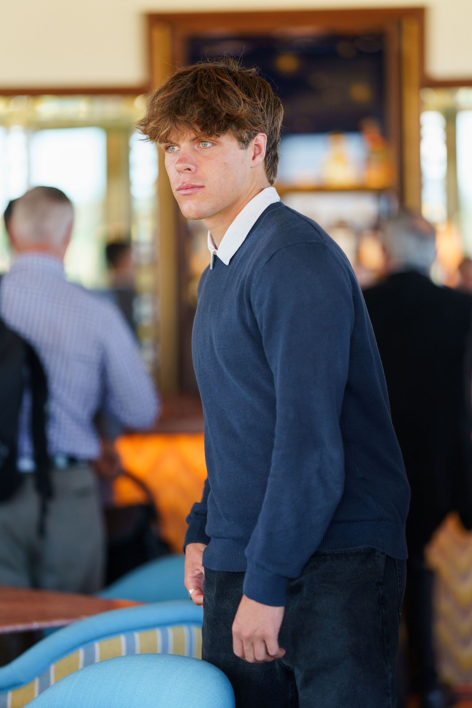 Person in navy sweater and white collar standing in an elegant indoor venue.