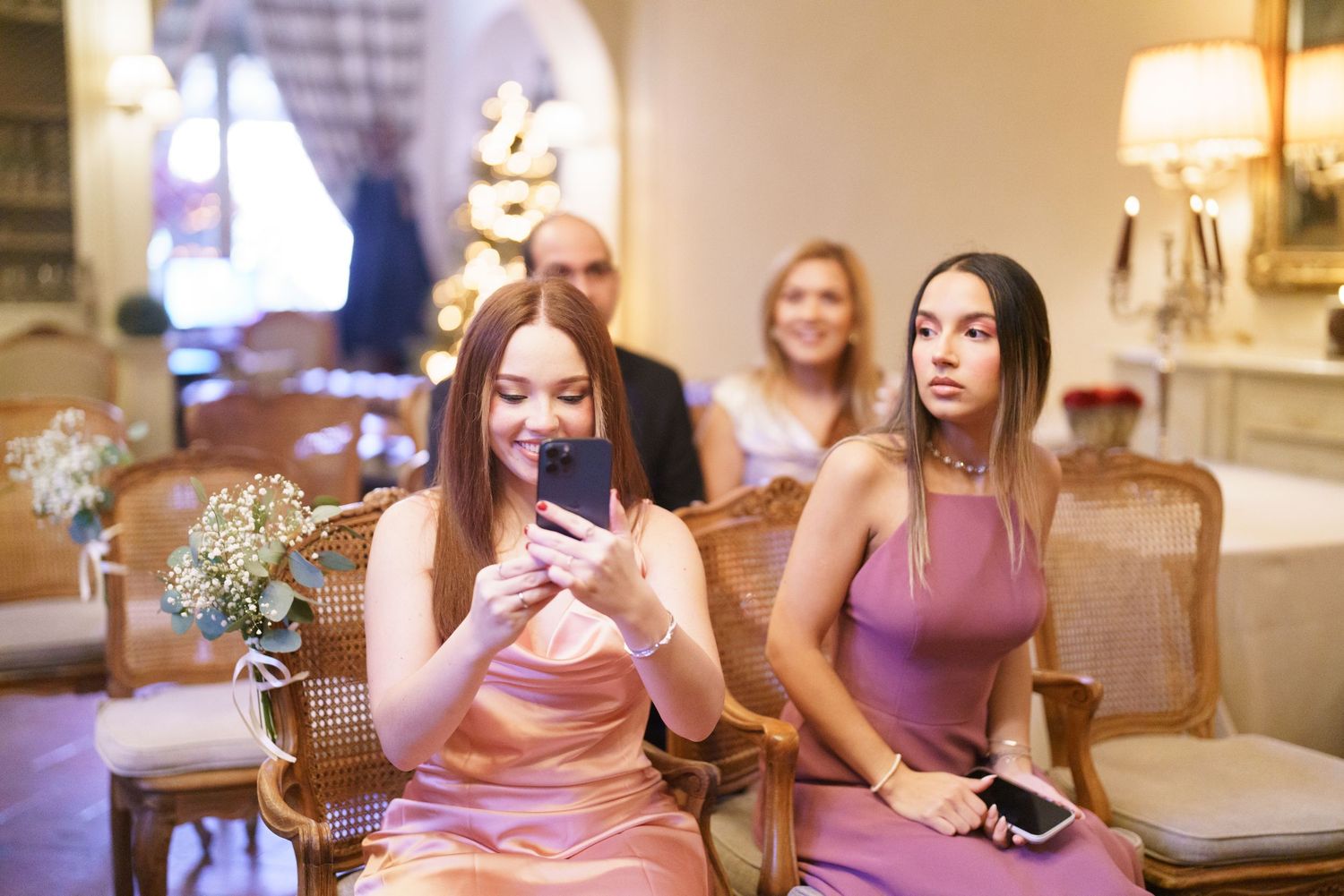 Bridesmaids in pink dresses gather for conversation at an indoor wedding reception.