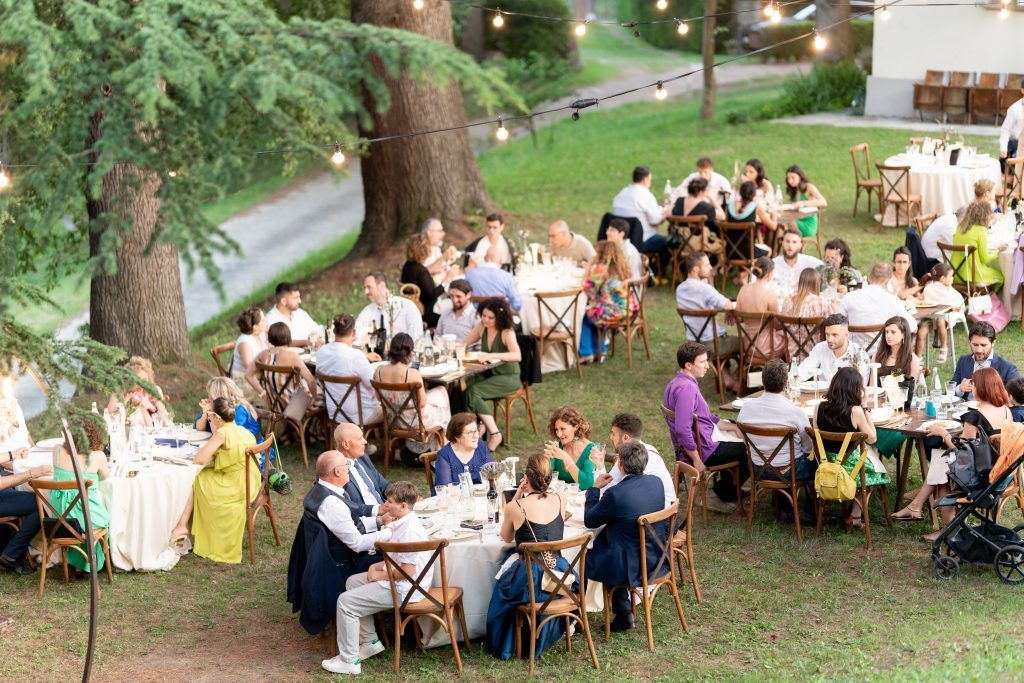 Long tables set up outdoors for a garden wedding reception with guests seated for dinner.
