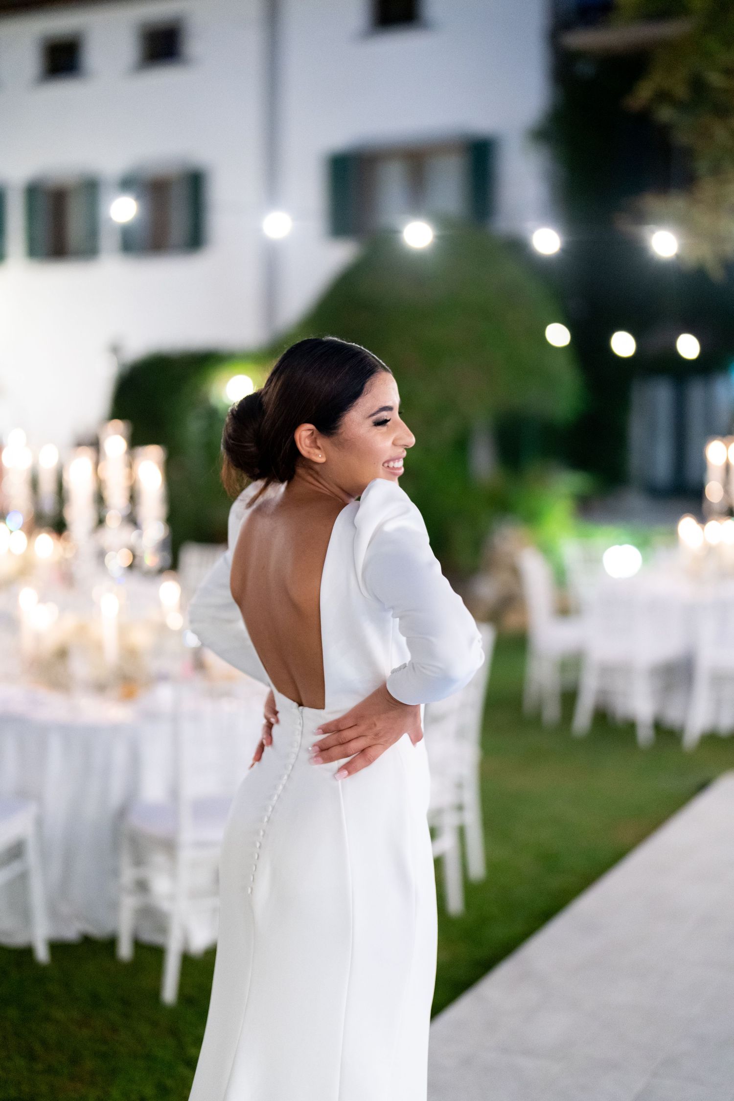 A white wedding gown with a dramatic open back design shown in an outdoor garden setting.