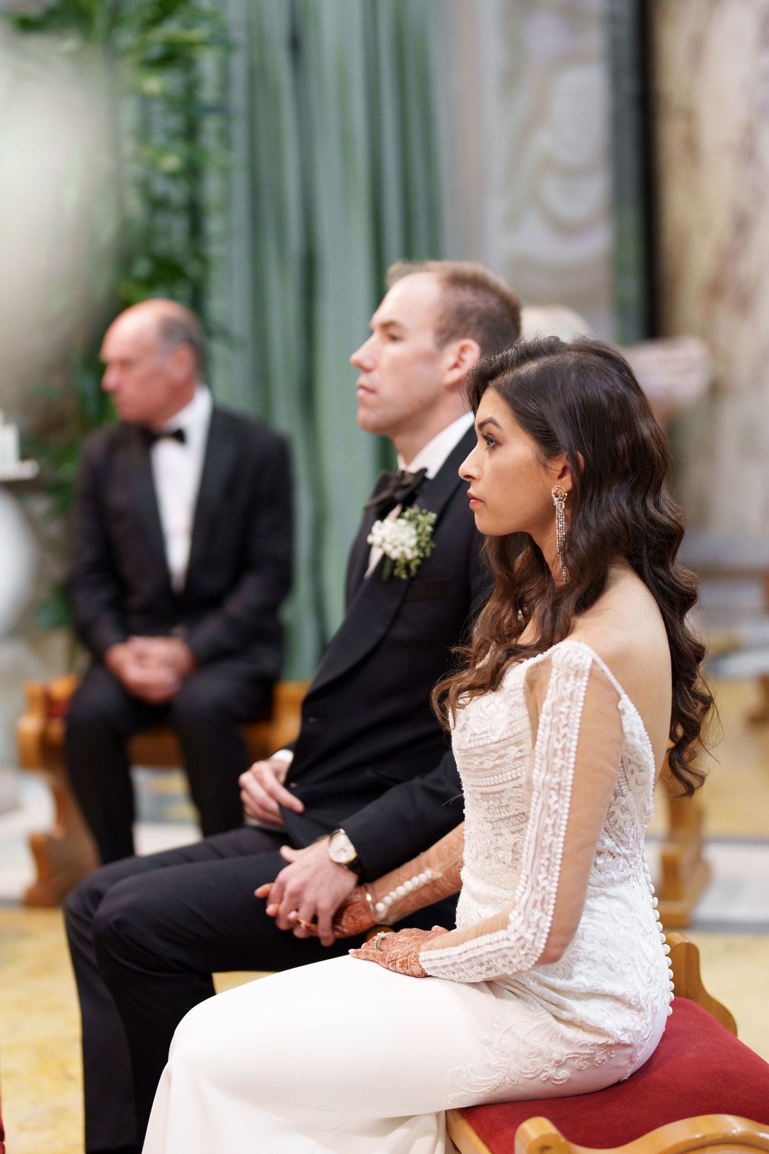 Wedding party seated on vintage furniture in formal attire during elegant indoor celebration.