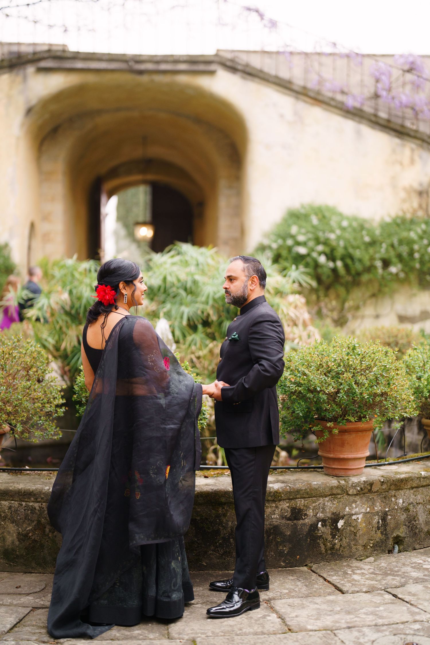 Couple in formal wear standing by garden terrace with stone archway.