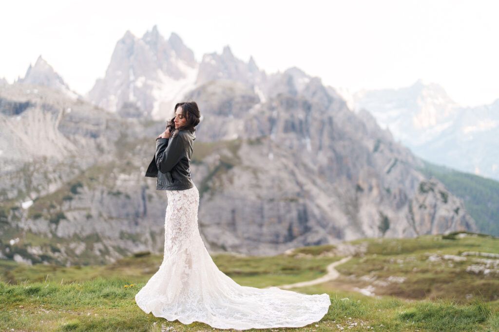 A flowing white wedding dress billows dramatically against rugged mountain peaks in the Dolomites.