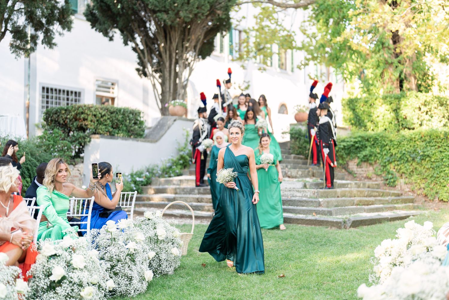 Wedding guests and military officers gathering for an outdoor garden ceremony.