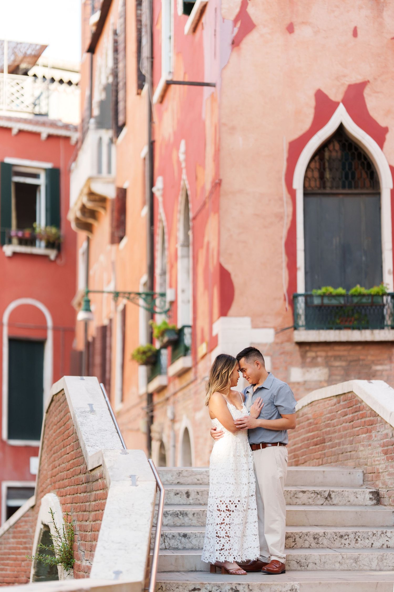 Romantic couple embracing on stone bridge steps in Venice, Italy, with colorful historic buildings in the background.