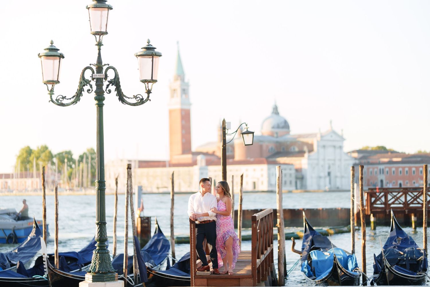Couple standing on a dock in Venice Italy with gondolas and San Giorgio Maggiore church in the background.