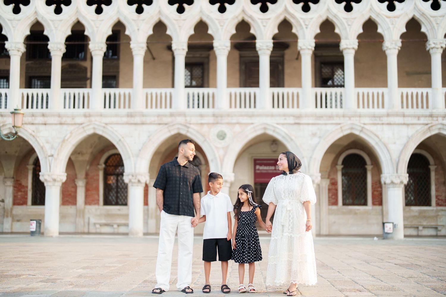 Family of four posing in front of ornate Gothic arches at Doge's Palace in Venice, Italy.