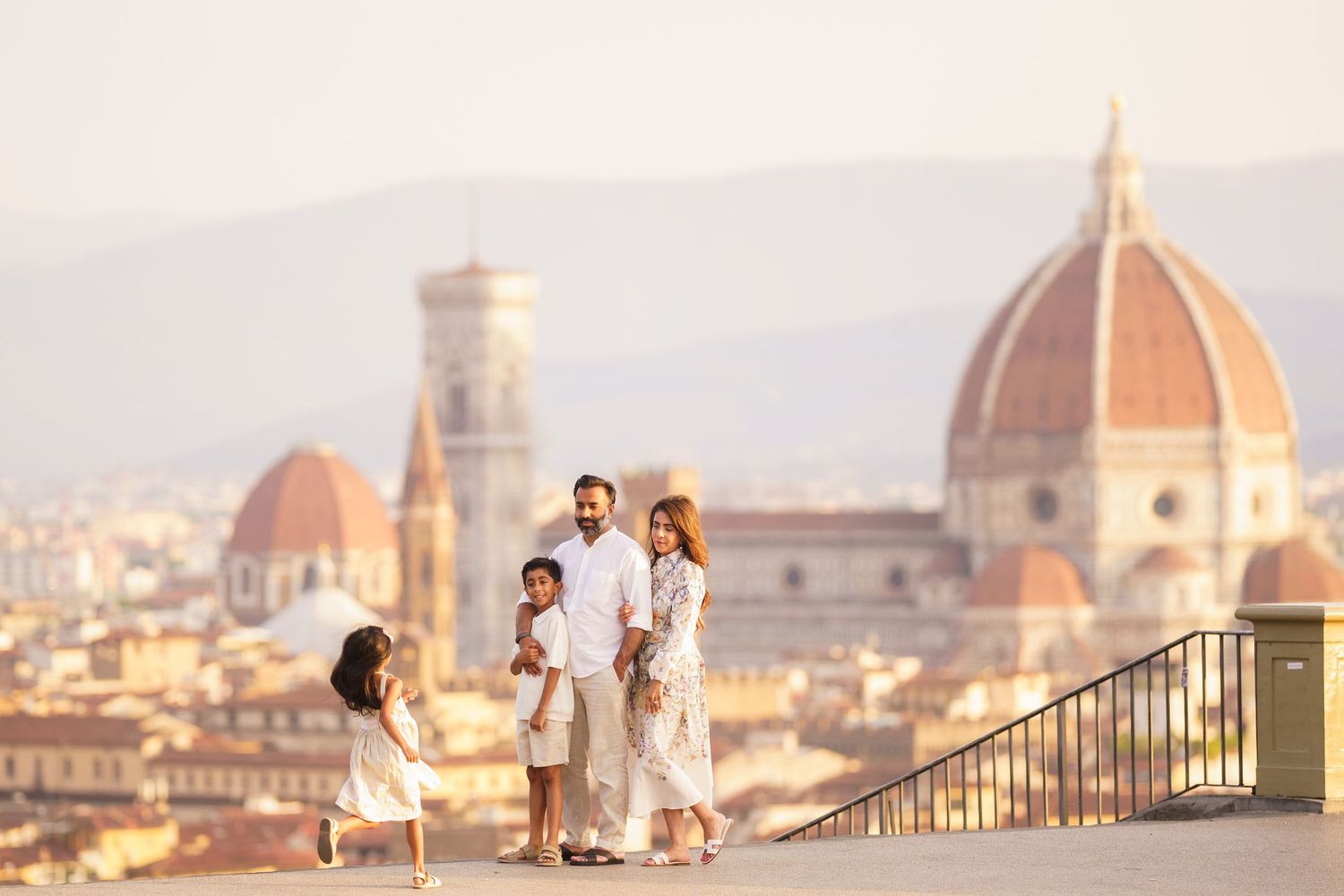 Family in white outfits posing before Florence Cathedral dome and cityscape at golden hour.