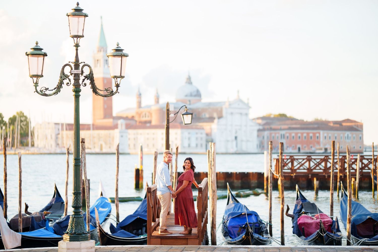 Romantic couple standing on a Venice dock with gondolas and San Giorgio Maggiore church in the background.