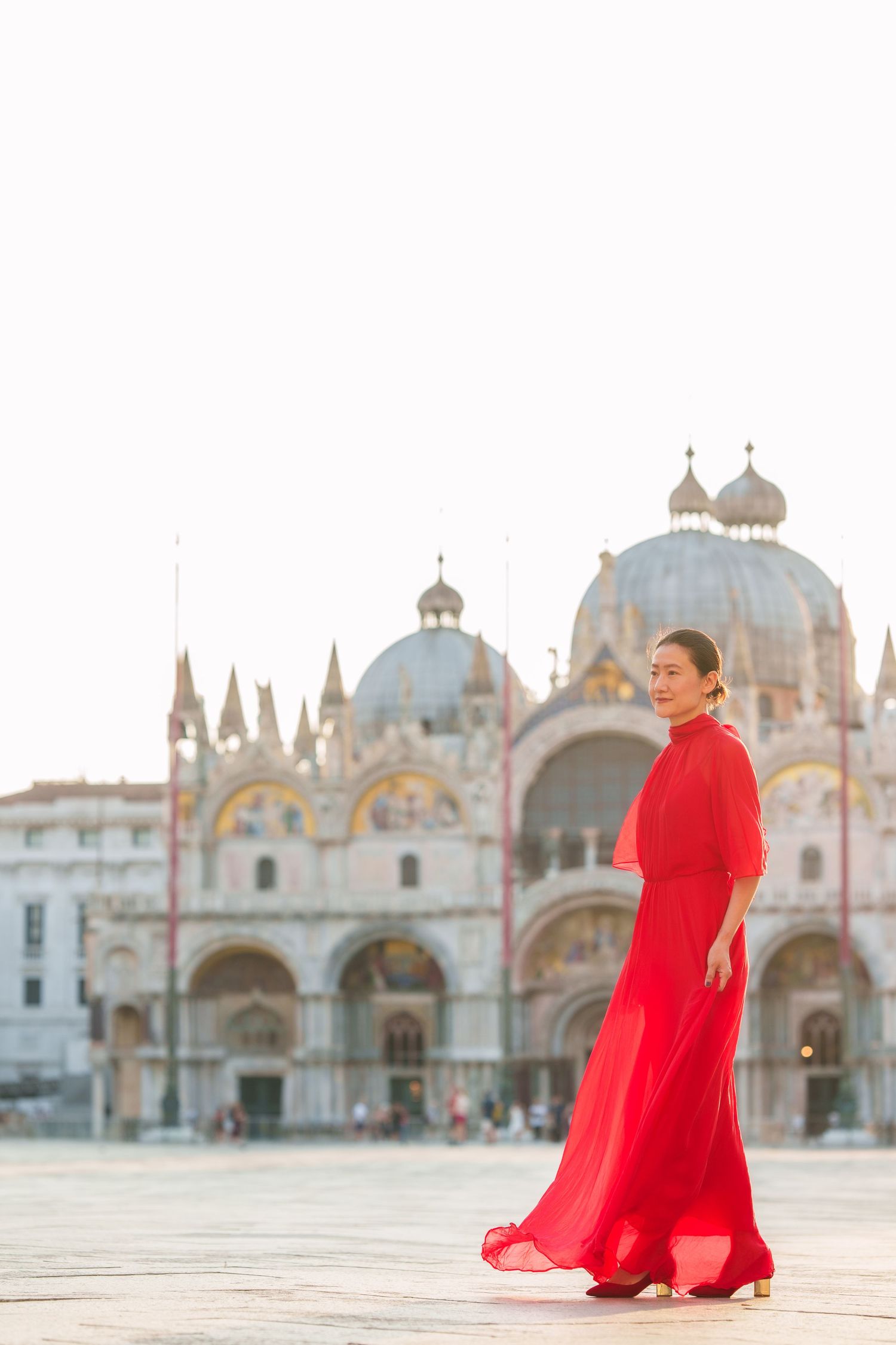 Woman in red dress posing in St. Mark's Square, Venice, with the iconic Basilica di San Marco in the background.
