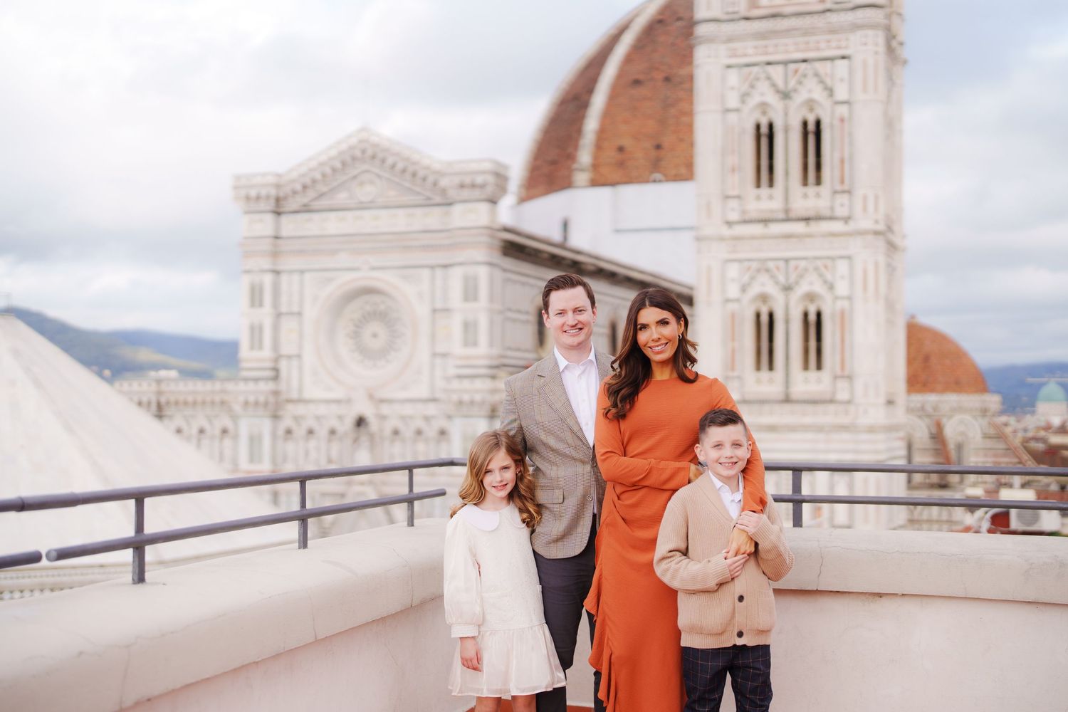 Family of four posing on a rooftop terrace with Florence Cathedral dome and Giotto's Campanile in background.