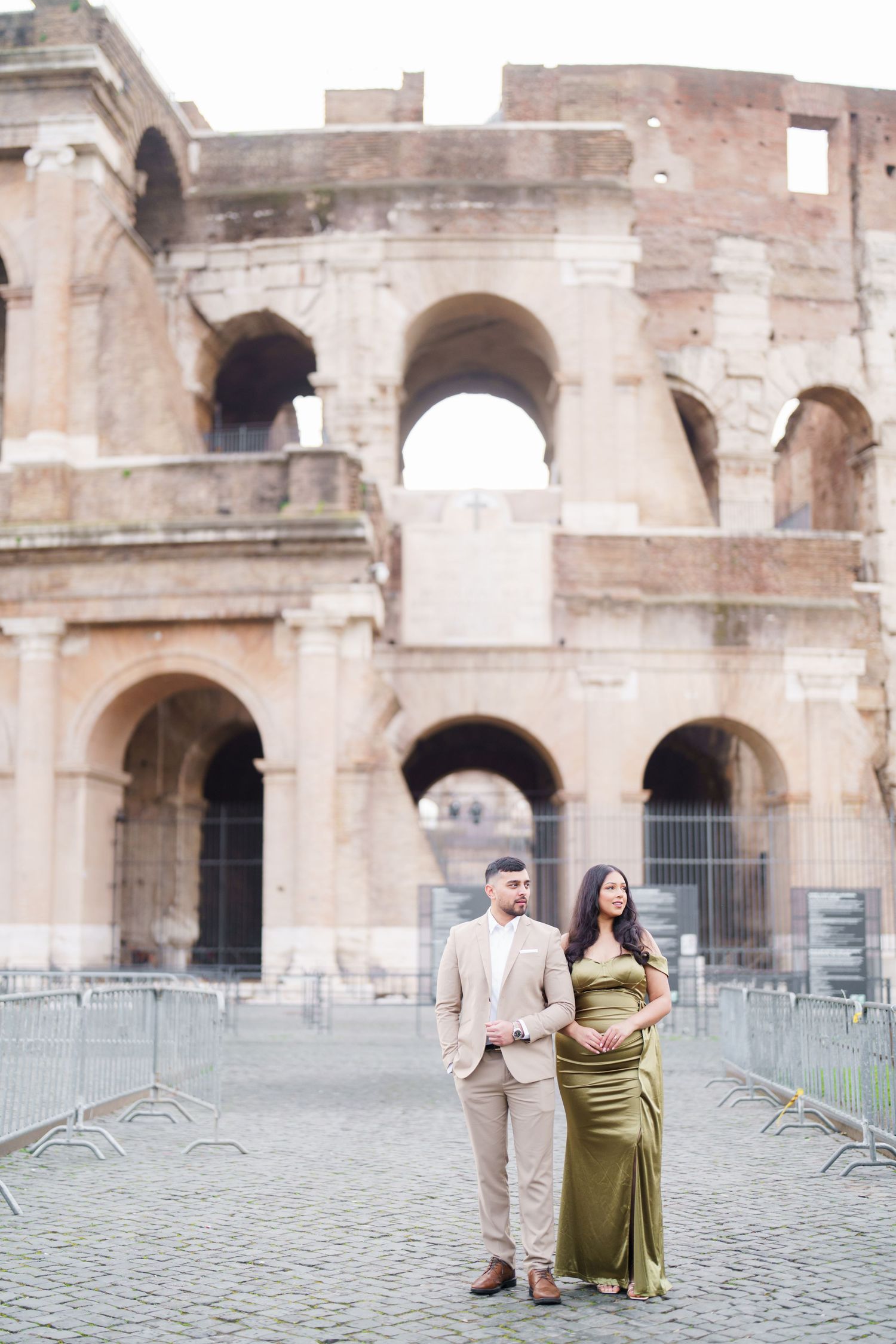 Couple posing in front of the Colosseum in Rome, man in beige suit and woman in elegant olive green gown.