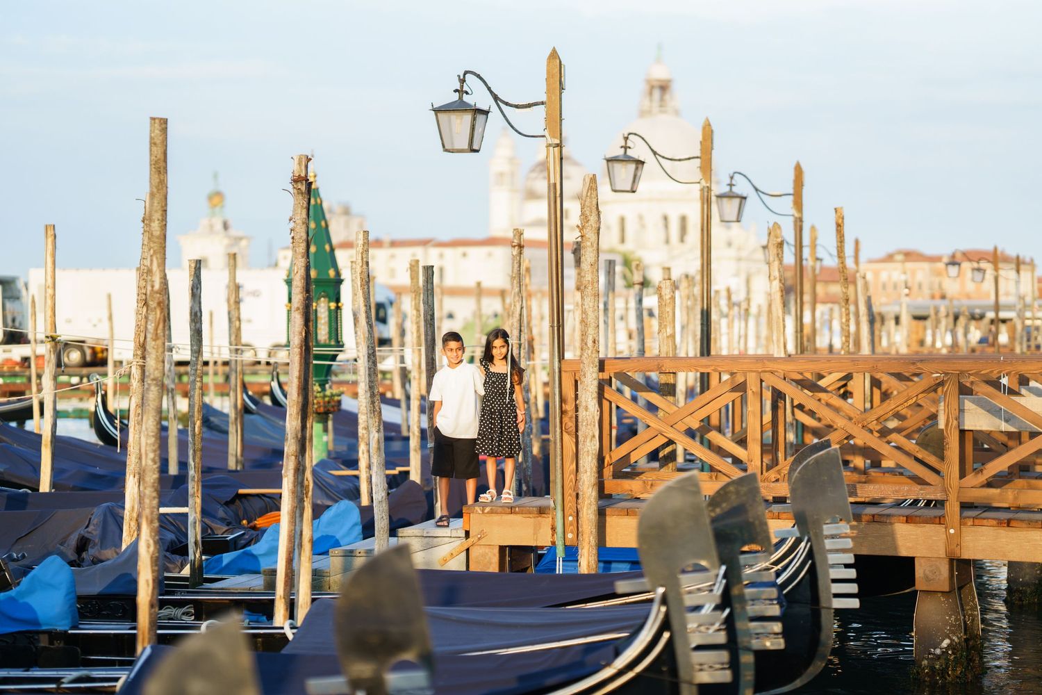Couple standing on a wooden dock among gondolas in Venice, Italy, with historic buildings in the background.