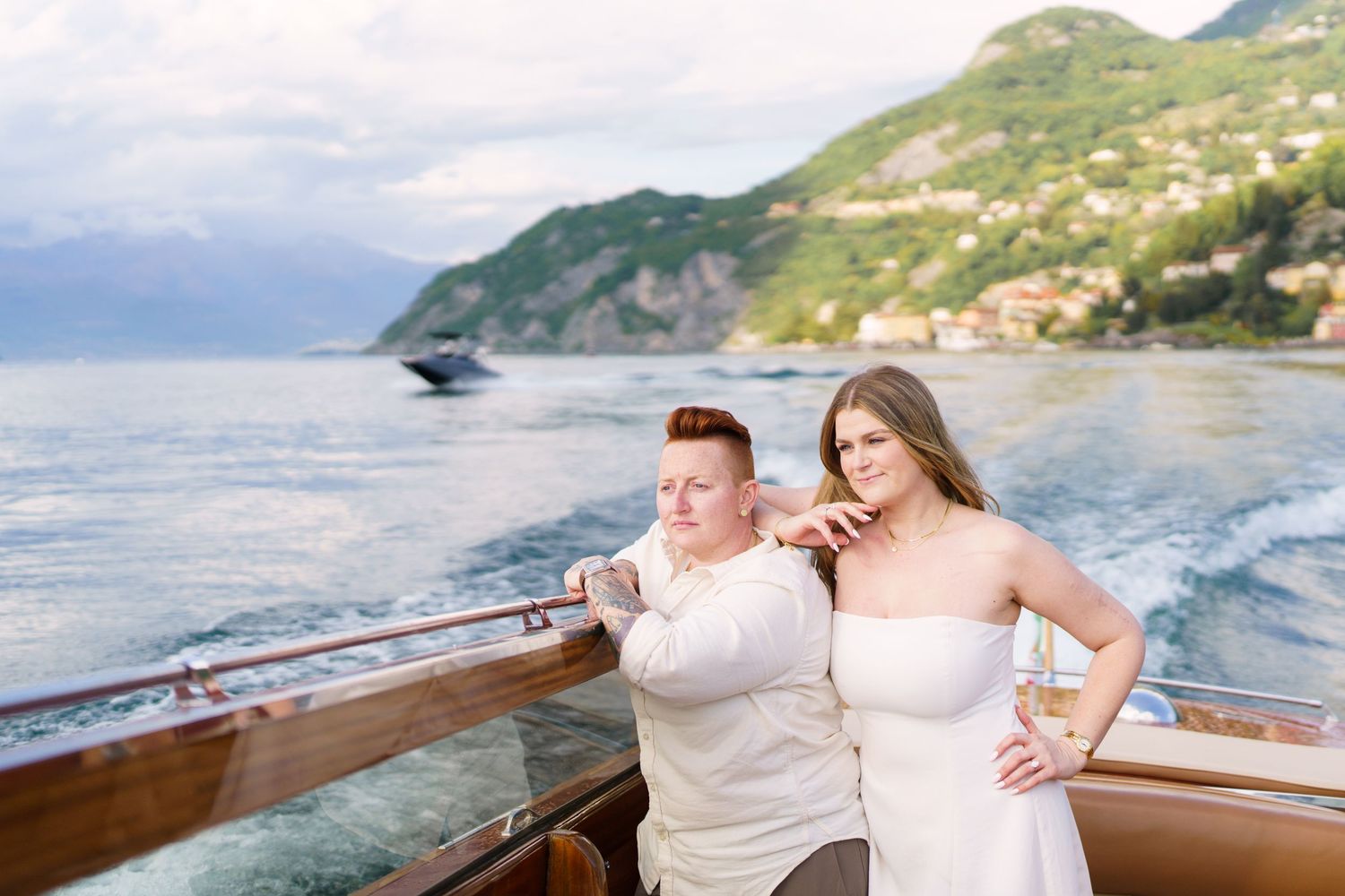 Couple posing on a luxury boat on Lake Como, Italy, with lush green hills and sparkling water in the background.