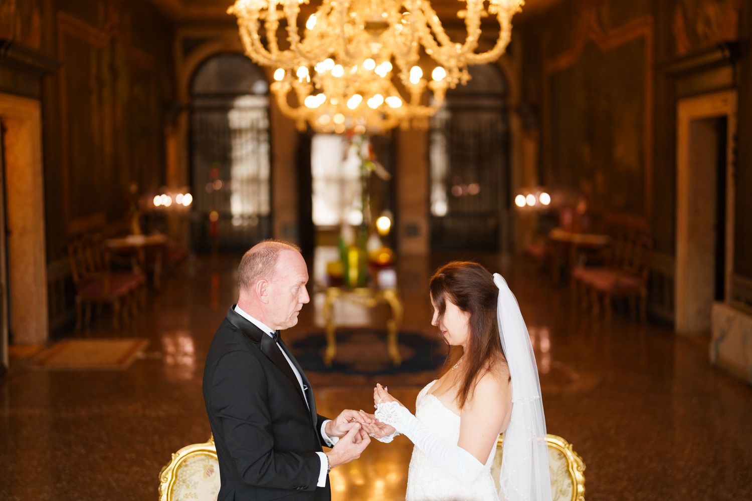 Couple dancing elegantly under ornate crystal chandeliers in a grand ballroom setting.