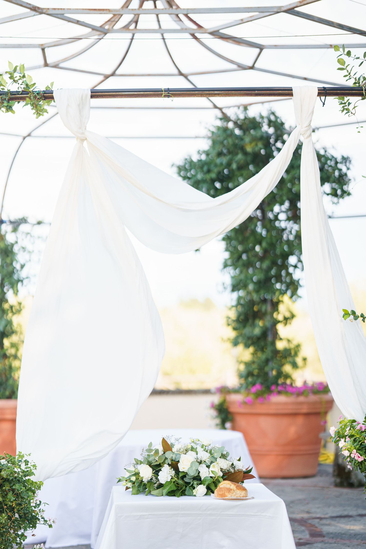 Sunlit outdoor space with white flowing curtains and terracotta planters creating an elegant atmosphere.