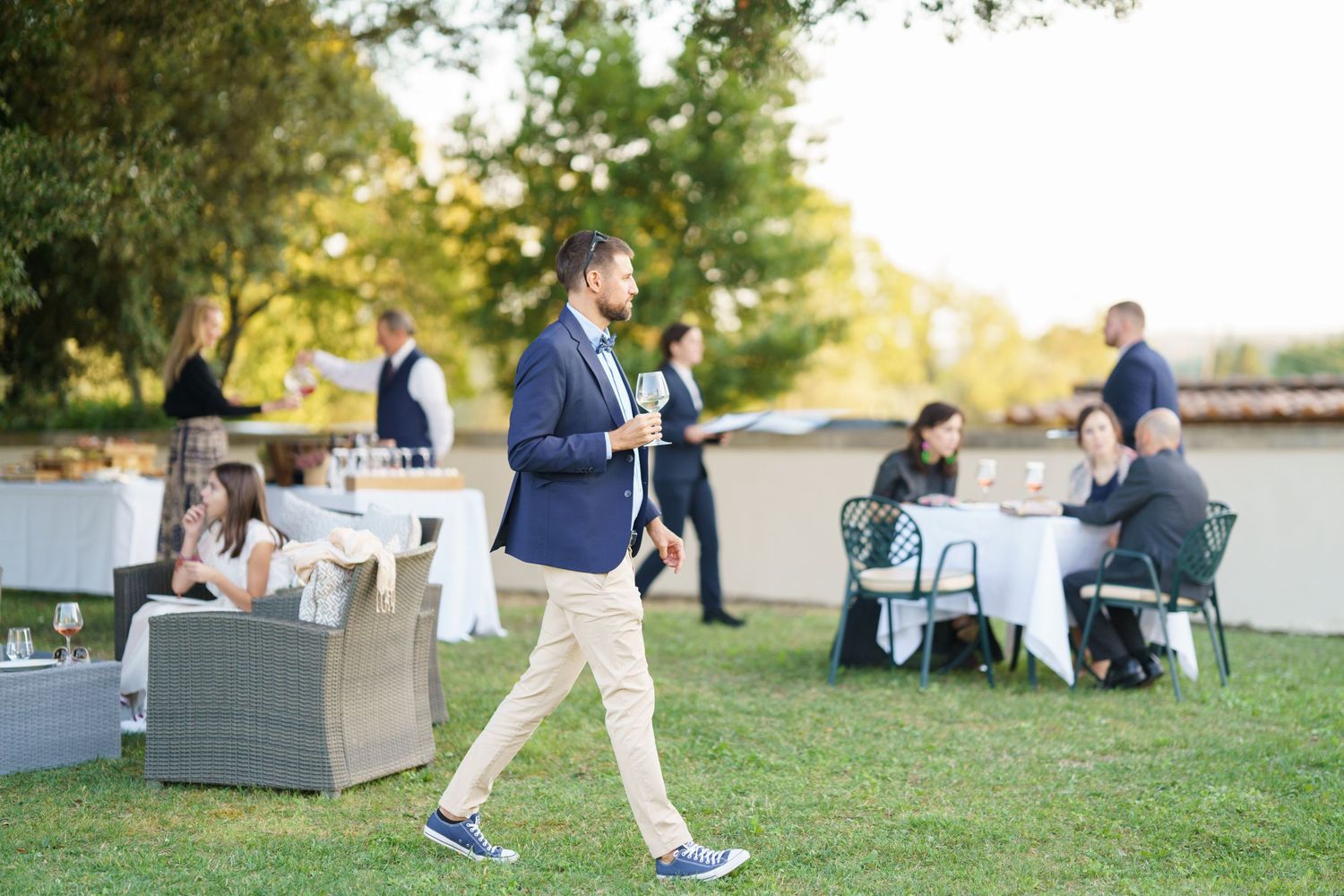 Guest walks across lawn at outdoor reception with dining tables in background.