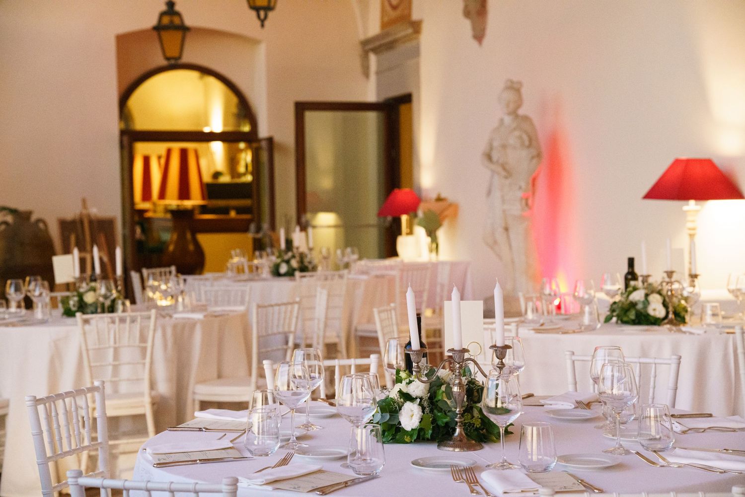 Banquet hall setup with white tables, hanging lanterns, and warm lighting for an elegant event.