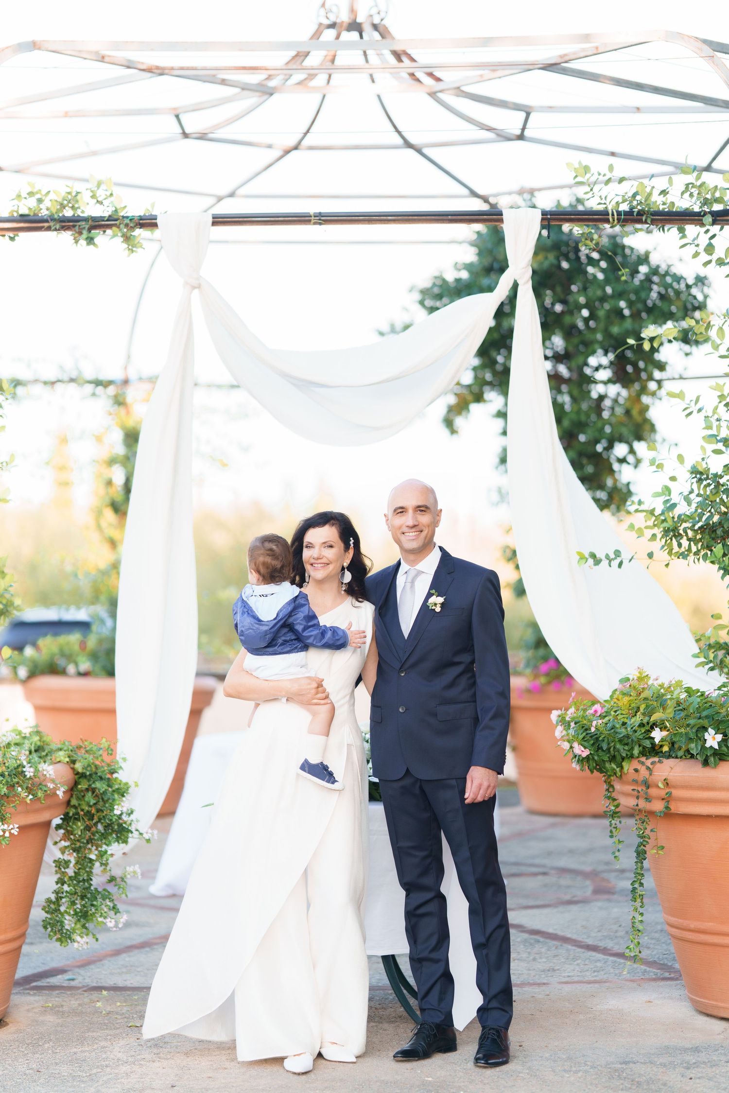 Wedding portraits under white canopy with decorative potted plants and soft natural lighting.
