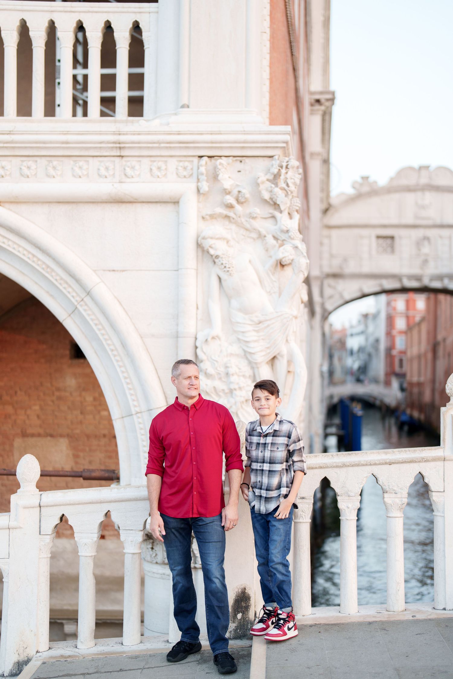 Two people stand on a bridge with ornate Venetian architecture and canals in the background in Venice, Italy.