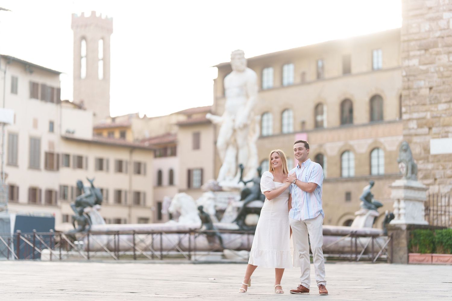 A romantic couple in white outfits strolls through the historic streets of Florence, Italy with ancient buildings behind them.