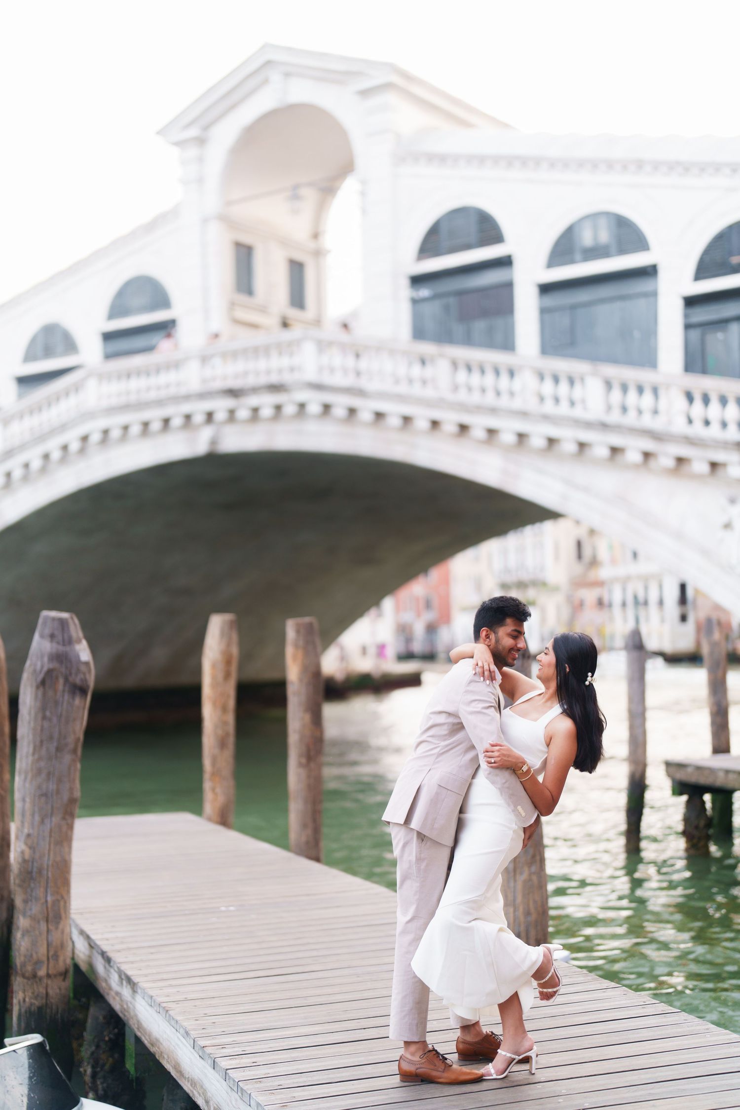 A romantic proposal moment on a wooden dock in Venice with the Rialto Bridge visible in the background.