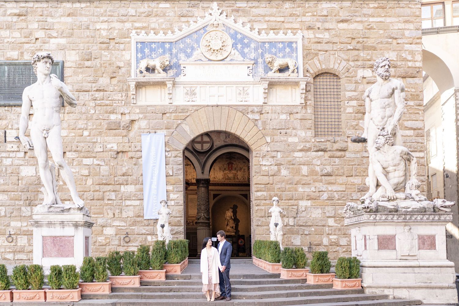 A couple stands between classical marble statues at the entrance of Palazzo Vecchio in Florence, Italy.