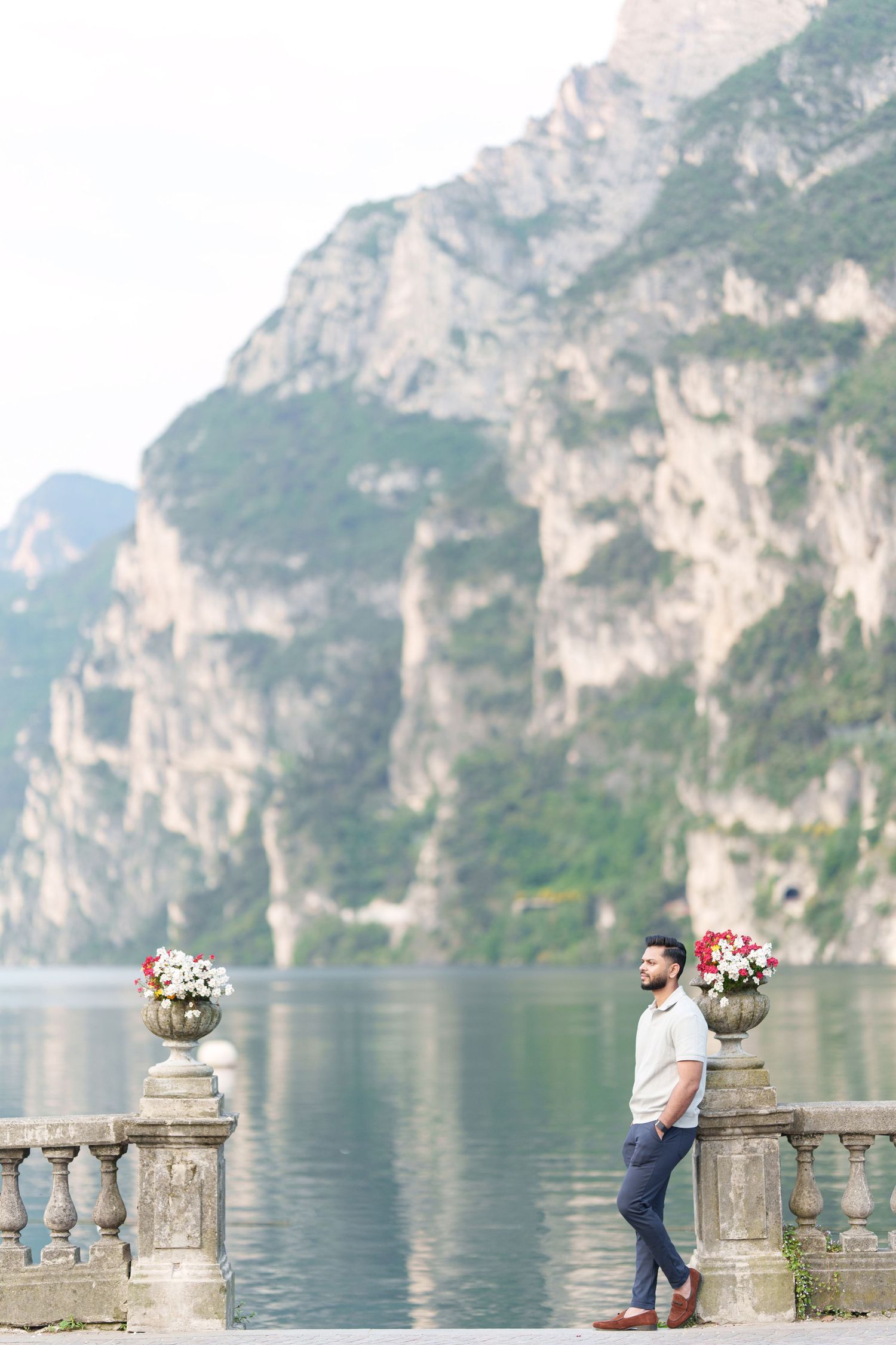 Scenic view of a person leaning on stone balustrade overlooking Lake Garda with towering cliffs in Italy.