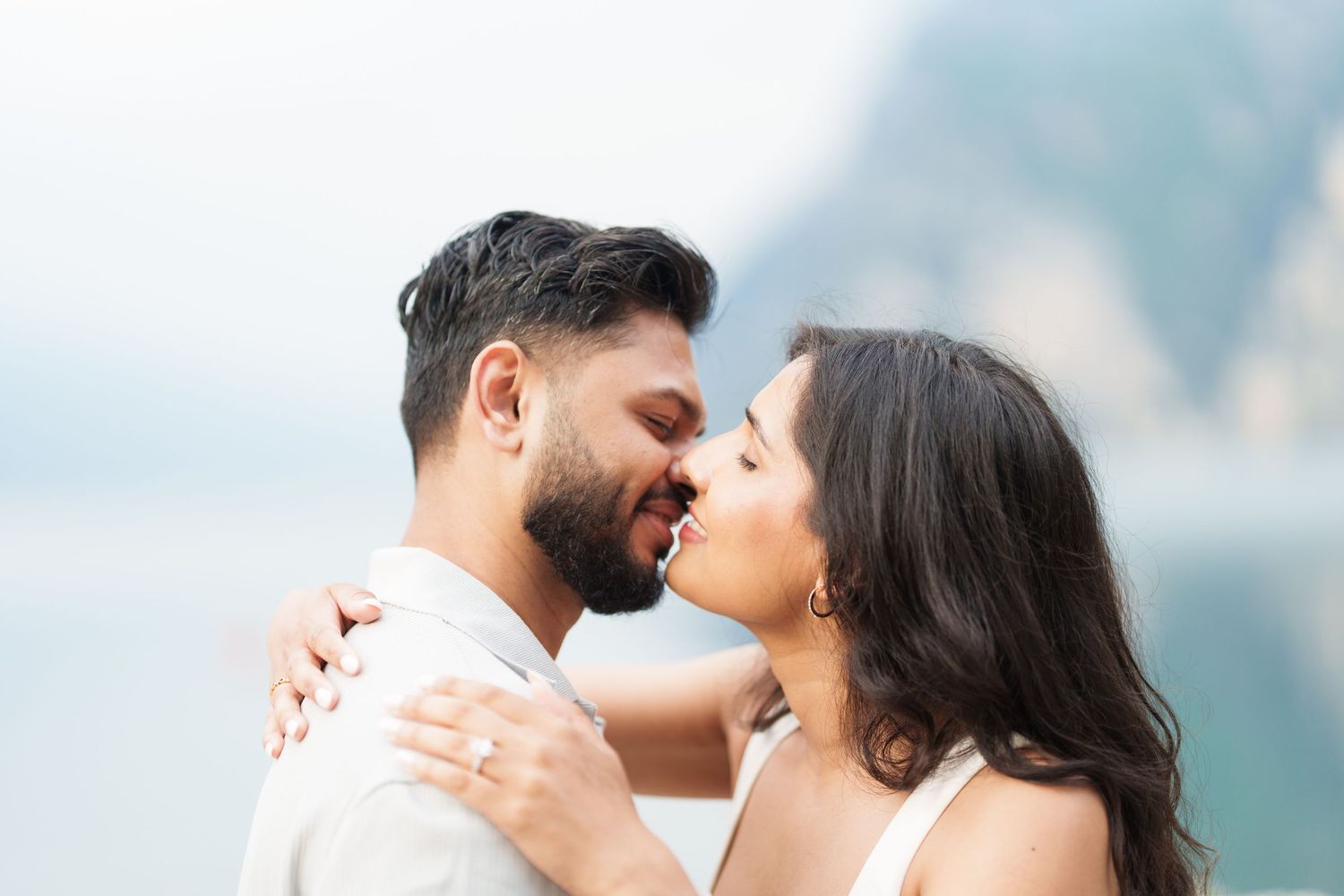 A romantic couple shares an intimate moment while embracing outdoors with a blurred natural backdrop.