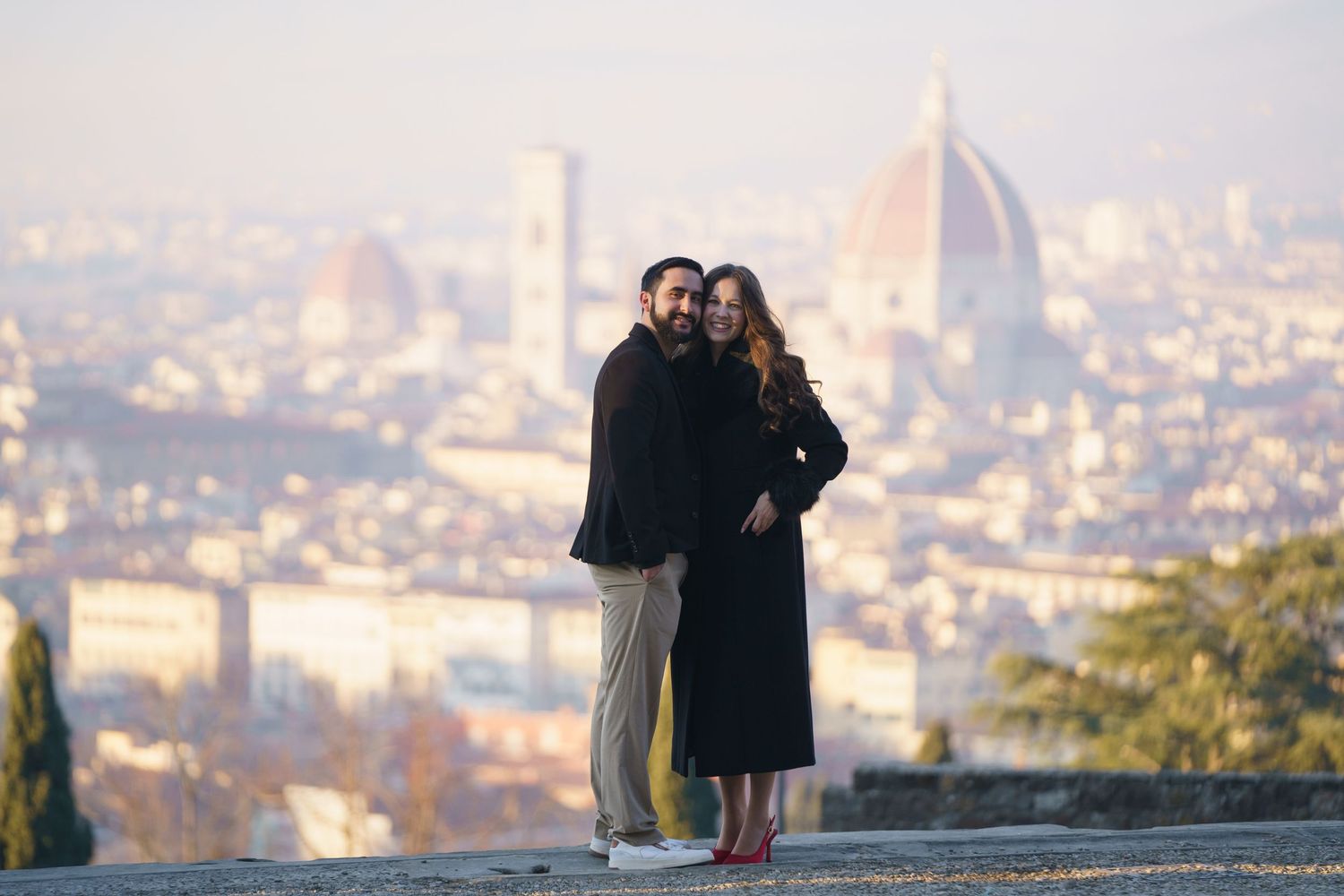 Two people embrace while enjoying a scenic overlook of Florence, Italy with the Duomo cathedral visible in the distance.
