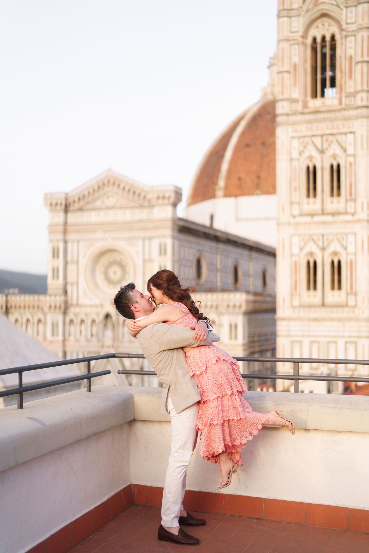 Romantic couple dancing on a rooftop terrace overlooking the historic Florence Cathedral during golden hour in Italy.