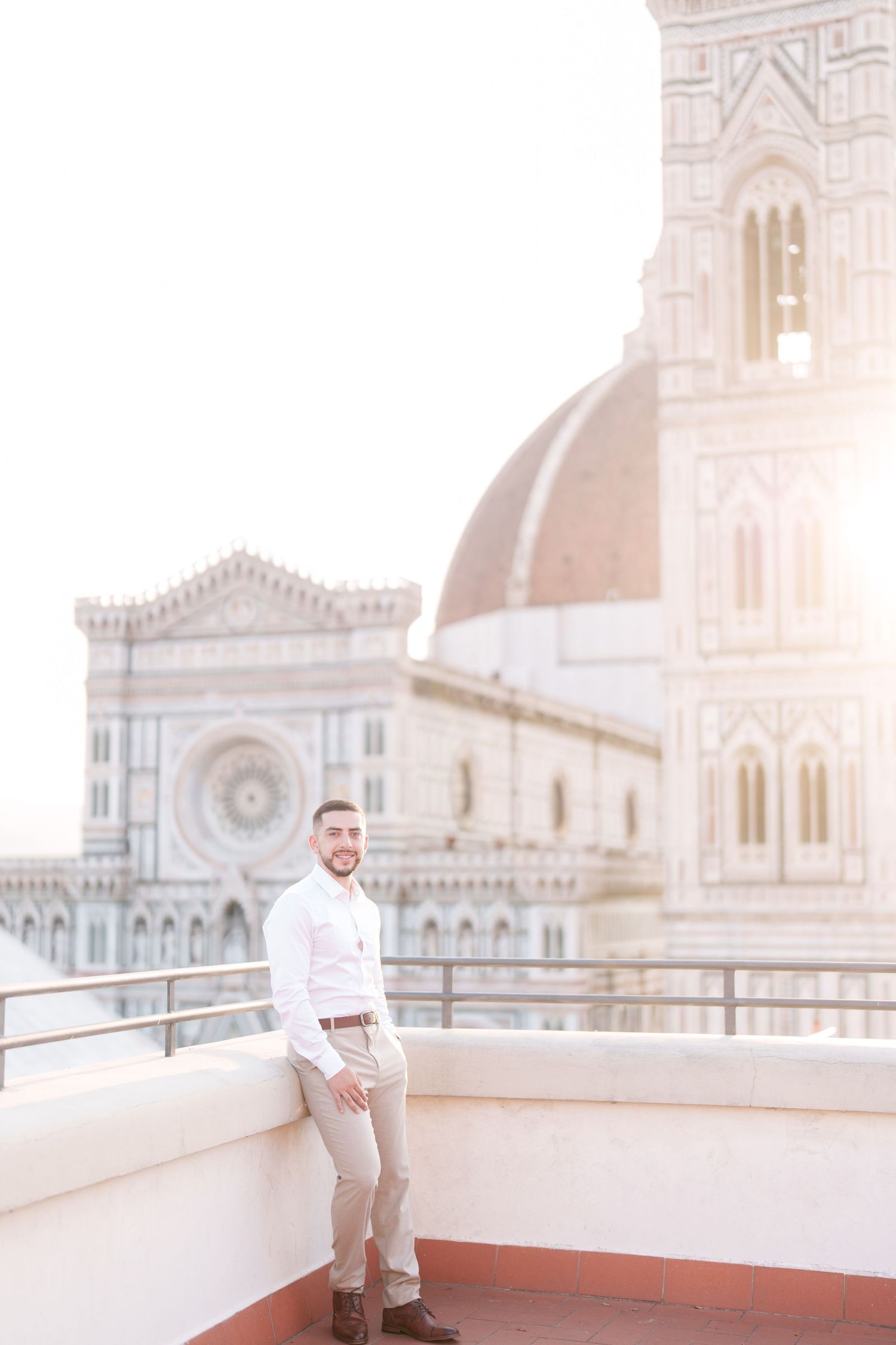 A person in white clothing stands on a rooftop terrace overlooking the historic Duomo cathedral in Florence, Italy.