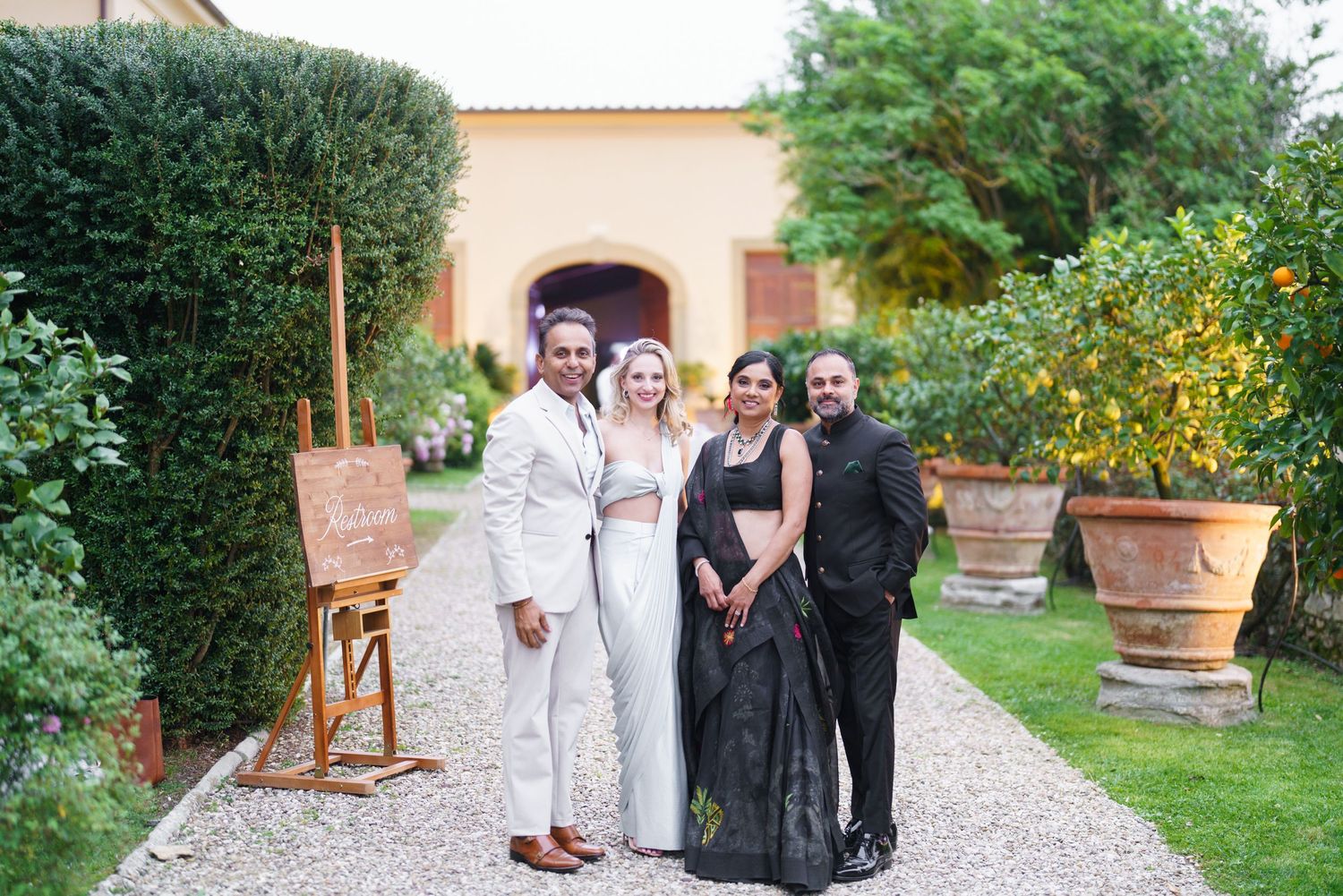 Wedding party poses together on garden path wearing mix of light and dark formal attire.